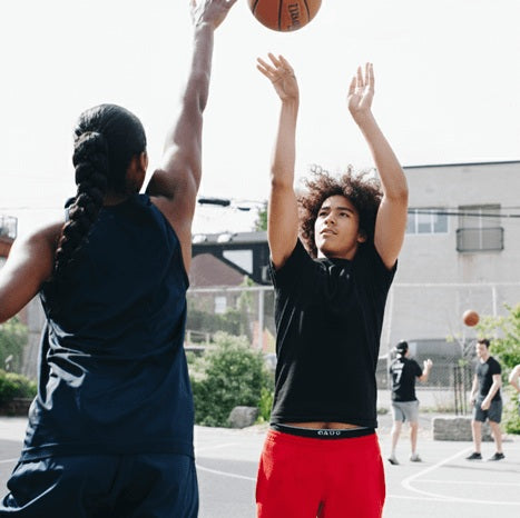 A parent helping her son practice basketball by guarding him.